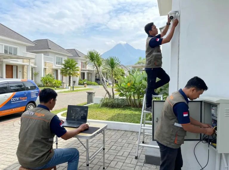 Tim teknisi CCTV Jogja melakukan instalasi kamera keamanan rumah dengan pengecekan sistem menggunakan laptop di area perumahan.